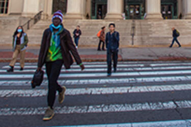 several people walking in a crosswalk on Massachusetts Avenue in front of MIT's building 10