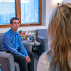 Full frame view of mental health clinician sitting in a comfortable chair and looking forward and to the right of the frame at a student, whose head and shoulders are visible from behind on the right side of the sr